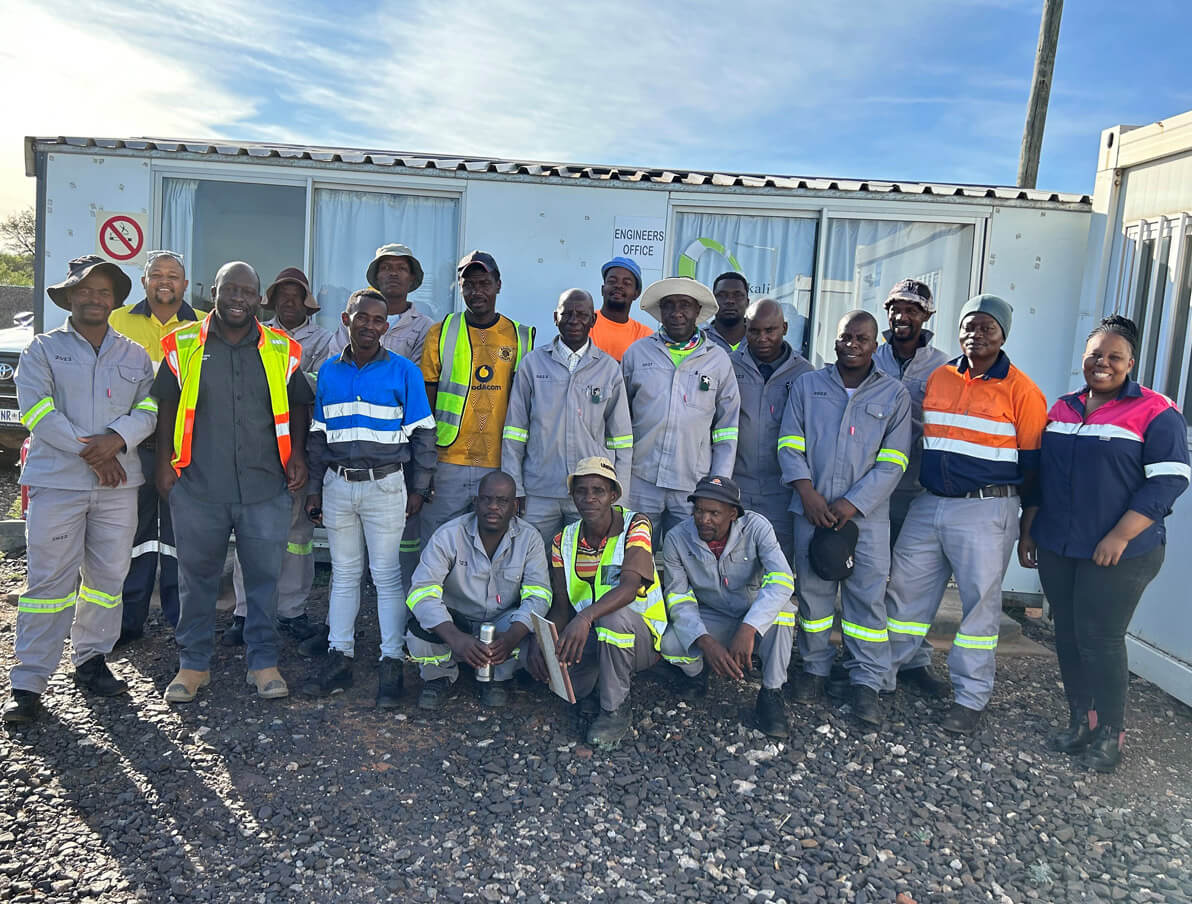 A group of men in work attire standing together, smiling for a photograph in a professional setting.
